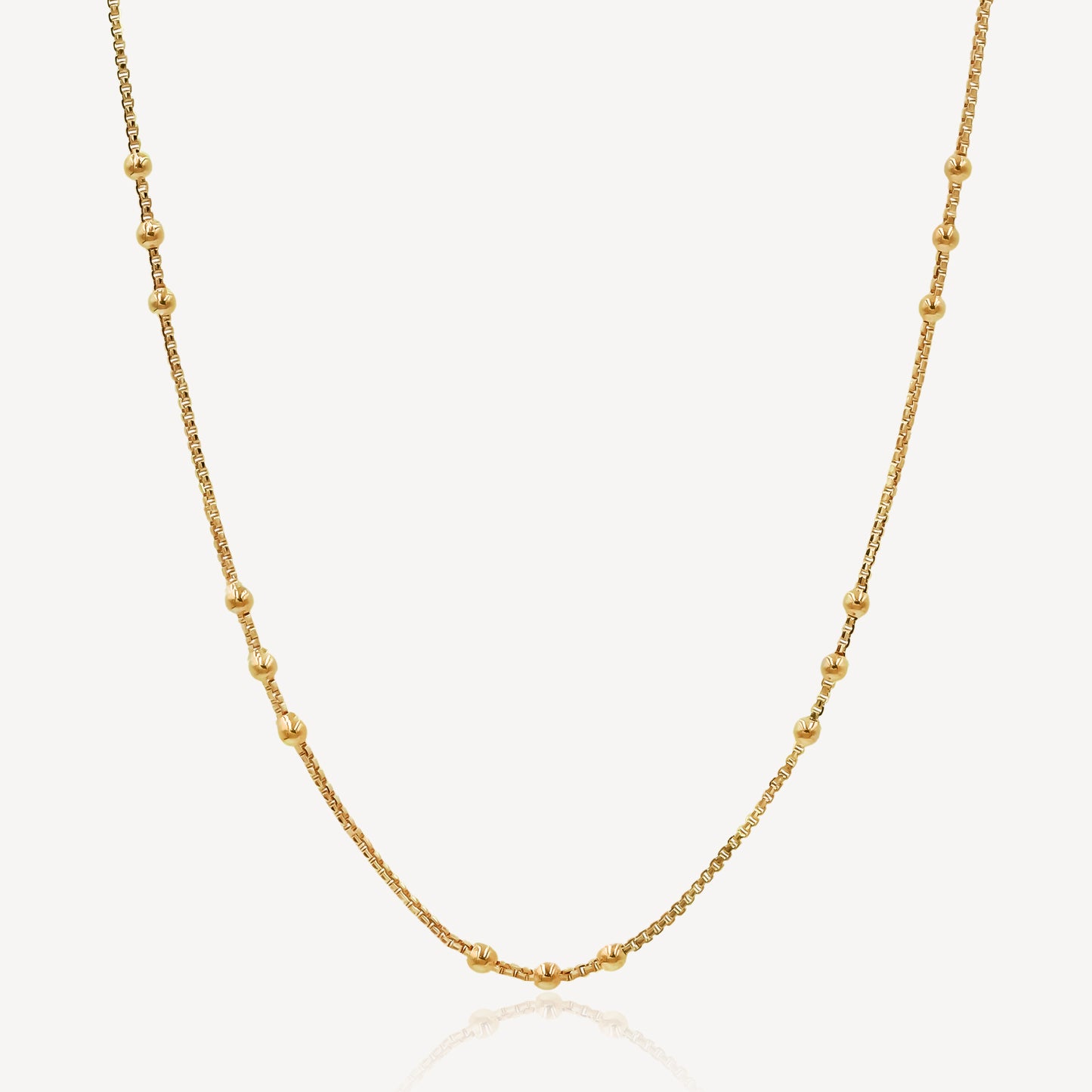 A gold-colored chain necklace with a series of uniform links and small embellishments, displayed against a white background.