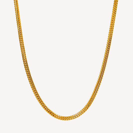 A gold dragon chain necklace laid out on a plain background.